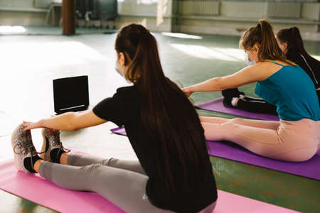 Group of multiracial wearing medical mask women train on mat in the gym during the pandemic. Online yoga fitness center for lifestyle design. Online class. Yoga exercise concept. High quality photoの写真素材