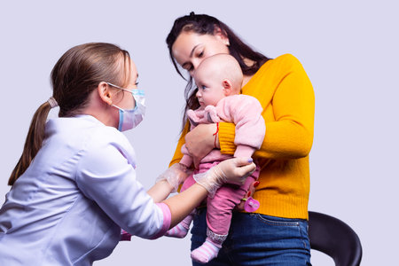 A mother with a baby on a medical inspection. A young doctor is examines a baby in a mask and...