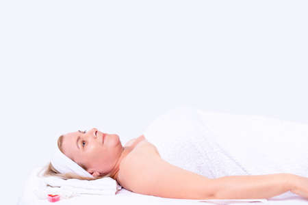Happy confident young lady with towel on her body waiting for cosmetologist to make a cosmetic treatment in spa salon clinic. High quality photoの写真素材