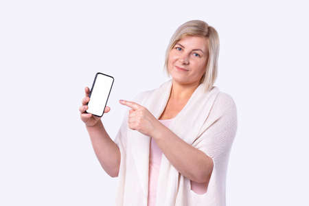 A blonde pretty woman in white cardigan wants to make photo of her after cosmetic procedures using smartphone. High quality photoの写真素材