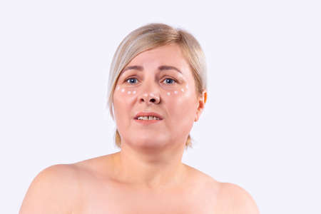 Beautiful woman with clean fresh skin goes through the cosmetic procedure with points from the cream on the face. High quality photoの写真素材