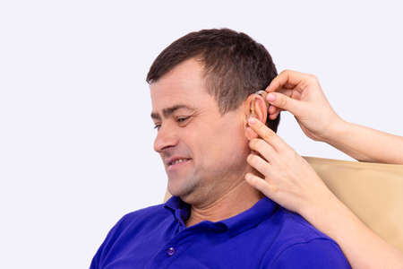 Otolaryngologist putting hearing aid in patient's ear while the patient sitting in the clinic cabinet. High quality photoの写真素材