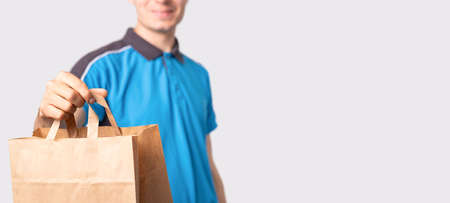 Delivery man in a blue polo shirt holding a package carton bag with handless pulling it forward and smiling.の写真素材