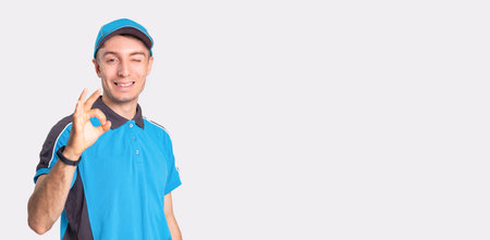 Photo of a smiling delivery man standing in front of camera showing with the gesture everything is...