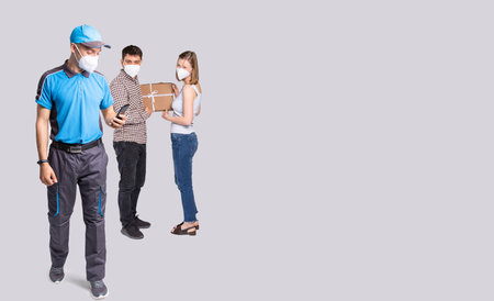 Courier with the mobile phone in the hand delivered a box during a pandemic time so they are wearing...