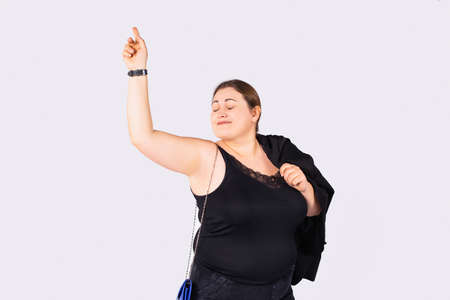 Woman in black shirt , jeans and blue purse on a chain with closed eyes is happy with herself raised one hand upの写真素材