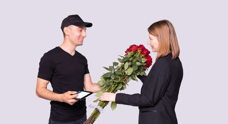 Business woman got a bouquet of flowers from the courier in black uniform and she need to sign for delivery.の写真素材