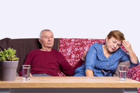 Adults are resting sitting on the sofa near the table with glasses of water at it because they are tired.の写真素材