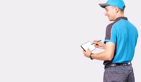 The courier in blue uniform makes order for the delivery of goods holding the pen and the tablet in his hands.の写真素材