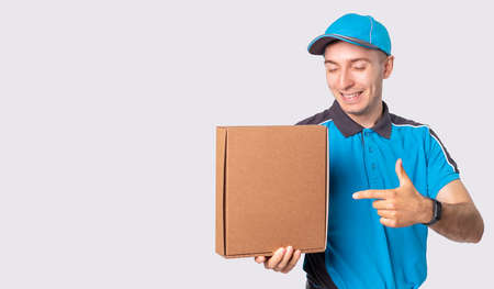 Smiling courier in blue uniform and a cap is pointing to the parcel he must deliver it to destination.の写真素材