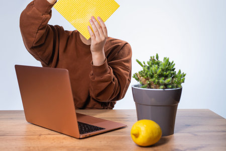 Young girl in brown sweater holding a yellow rag to wipe the table and the notebook then water the...