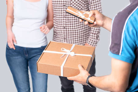 Courier holding smartphone while making delivery and makes photo of a parcel tied with a gift white ribbon.の写真素材