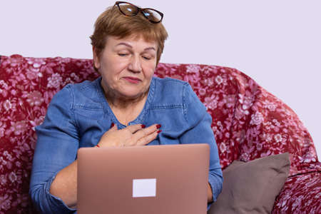 An old woman wearing glasses on her head sitting on the couch and talking online to her relatives abroad.の写真素材
