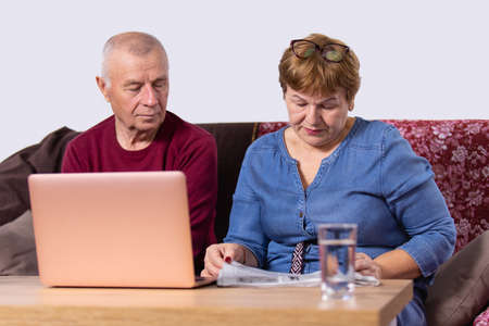Aged couple going about their business, woman reading a newspaper and man opened laptop and sitting near his wife.の写真素材