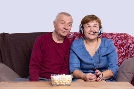 Retirement couple are sitting together on a couch, woman wearing headphones speaking into the microphone.の写真素材