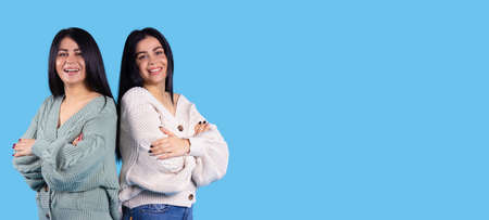 Banner, long format. Two smiling pretty young twins sisters girls standing back to back isolated on a blue background.の写真素材