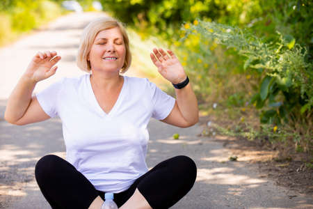 A woman in white t-shirt and black leggings sitting on yoga position outdoors doing meditation with hands keeping up.の写真素材
