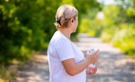 Side photo back of a strong blonde woman takes care of her health jogging in the morning holding a bottle of water and using headphones.の写真素材