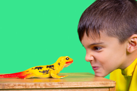 The boy short cut in yellow shirt is looking intently at a dinosaur toy putting his chin at the table.の写真素材