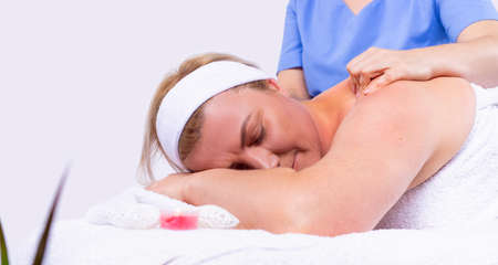 Specialist making shoulder massage to an adult woman relaxed and lying with closed eyes in a beauty salon .の写真素材