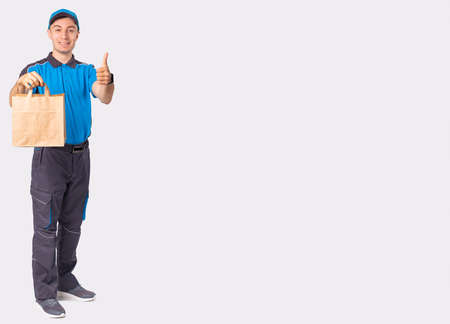 The full-length photo of a man courier poses with the cardboard bag with handless and putting his thumb up, everything is ok.の写真素材
