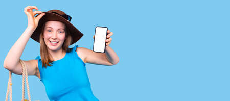 Pleasant young woman in a hat and wearing blue blouse holding the smartphone and holds on the brim of the hat.の写真素材