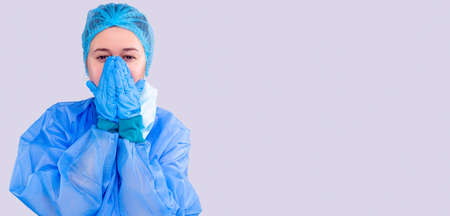 Woman medical assistant in medical equipment covers her exhausted face with her hands, she has no force.の写真素材