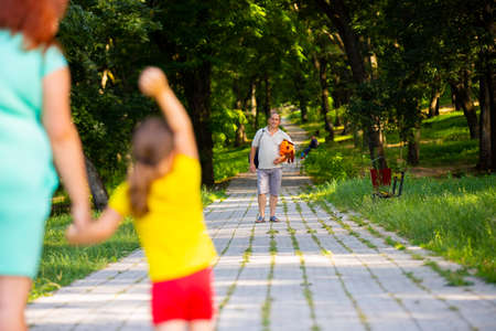 Daddy day came and mother with little daughter outdoors are looking at him in the distance, little girl is waving to him and daddy standing with the bag and a toy for his lovely daughter.の写真素材