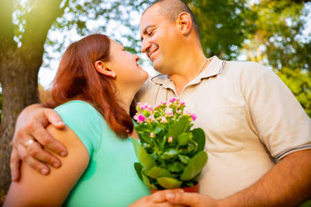 Close up photo of a happy couple in love is hugging being in the park together, husband gave his wife the flowers in the name of love.の写真素材