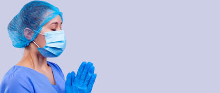 The woman doctor in blue medical uniform and mask with closed eyes is praying a quick recovery of the people.の写真素材