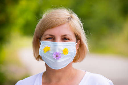 Close up portrait of a woman outdoors wearing medical face mask with flowers takes care of her body on summer in pandemic time.の写真素材