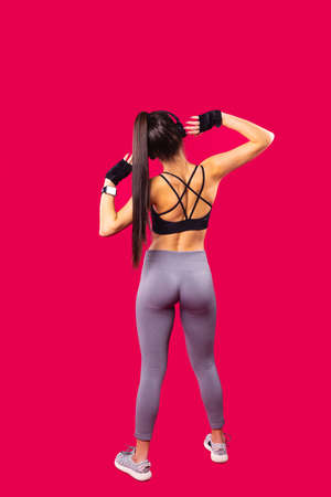 Back view of athletic beautiful young sexy woman wearing leggings and short top with cross straps on the back, listening the music using headphones.の写真素材
