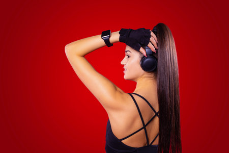 Back view of fitness young sexy woman with long hair ponytail holding the headphones with the hand and beautiful manicure.の写真素材