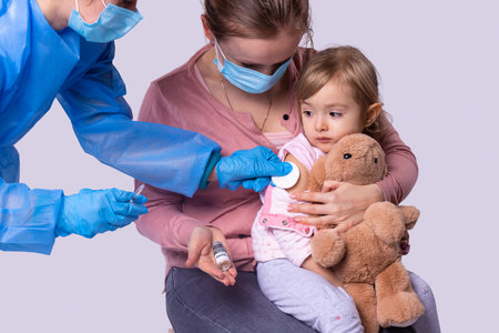 In pandemic time mother in medical face mask came with her little daughter to the doctor to put little kid girl vaccine.の写真素材