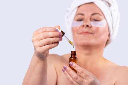 Close up photo of a grown nice woman with well-groomed hands and bright pink manicure holding a little bottle of essential oil.の写真素材