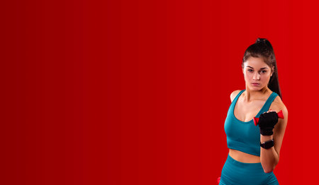 Young fitness girl with squinted eyes having one dumbbell in her hand practicing running indoors for health being.の写真素材