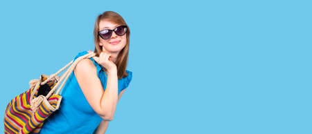 Happy smiling woman wearing light blue blouse in sunglasses holding the bag with color stripes on the back.の写真素材