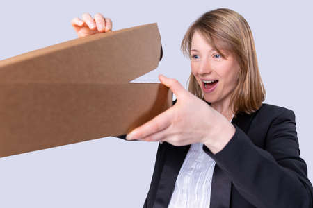 Business blonde lady wearing the black jacket received the cartoon package and opening it with satisfied face looking.の写真素材