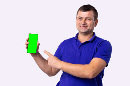 Portrait of happy fashionable handsome man in a blue shirt look at camera holding cellphone and pointing at it. High quality photoの写真素材