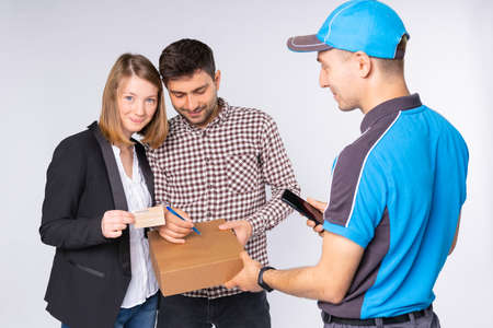 The man courier delivers home the box to the business lady with the husband, he signs for the delivery service and the wife paying using the card. High quality photoの写真素材