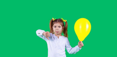 Young girl holding yellow balloon with angry face, negative sign showing dislike with thumbs down, rejection concept.の写真素材