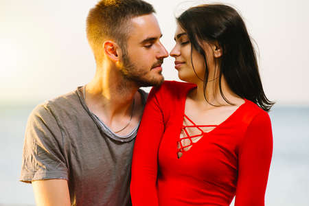 Beautiful young couple in love, the man looking at his pretty girlfriend in red sexy dress with love and she closed her eyes with delight.の写真素材