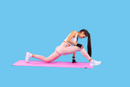 Girl with long ponytail in sports clothes and shoes practicing fitness exercises doing lunges forward on the pink mat.の写真素材
