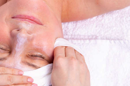 Close up side view photo of a woman getting facial care by beautician at spa salon, applies a cream mask to the face then takes it off.の写真素材