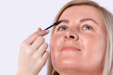 Caucasian pretty woman with brilliant face tone does procedures for combing eyebrows with a brush in a beauty salon.の写真素材