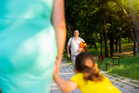 Back view photo of mother and little girl can not wait for her daddy to spend together the hole day in the park and he is going to meet them holding a soft dog toy for his daughter.の写真素材