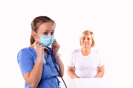 The woman doctor in uniform, medical mask and protective gloves pits on a stethoscope to listen to the patient breathing.の写真素材