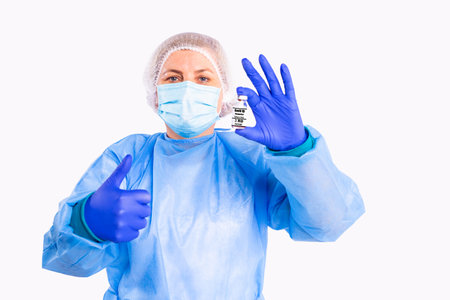 The photo of a doctor in medical uniform, protective face mask and gloves holding in one hand vaccine bottle against coronavirus and with another hand makes sign ok.の写真素材