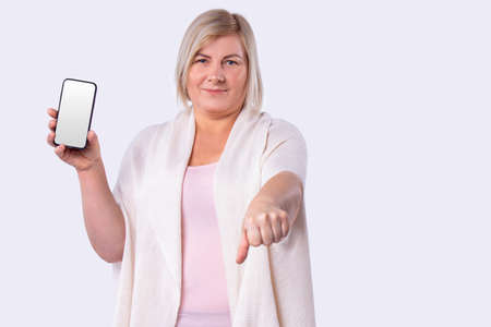 Smiling woman cut blond hair in a white long cardigan holding mobile phone and reached out into a fist.の写真素材