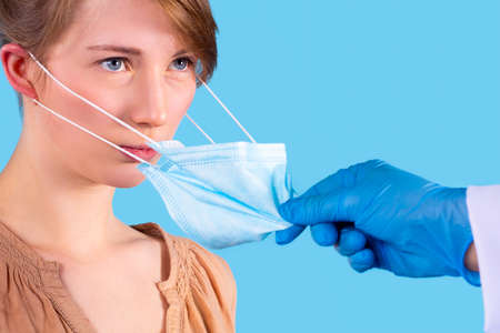 Photo of a serious woman with blue eyes looking at the doctor attentively while he takes off the medical face mask wearing protective gloves.の写真素材